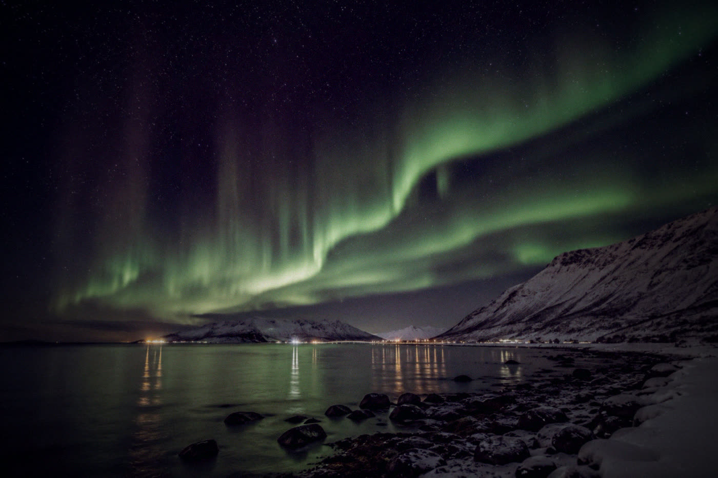 Green aurora arc above the Lyngen Alps and a calm fjord