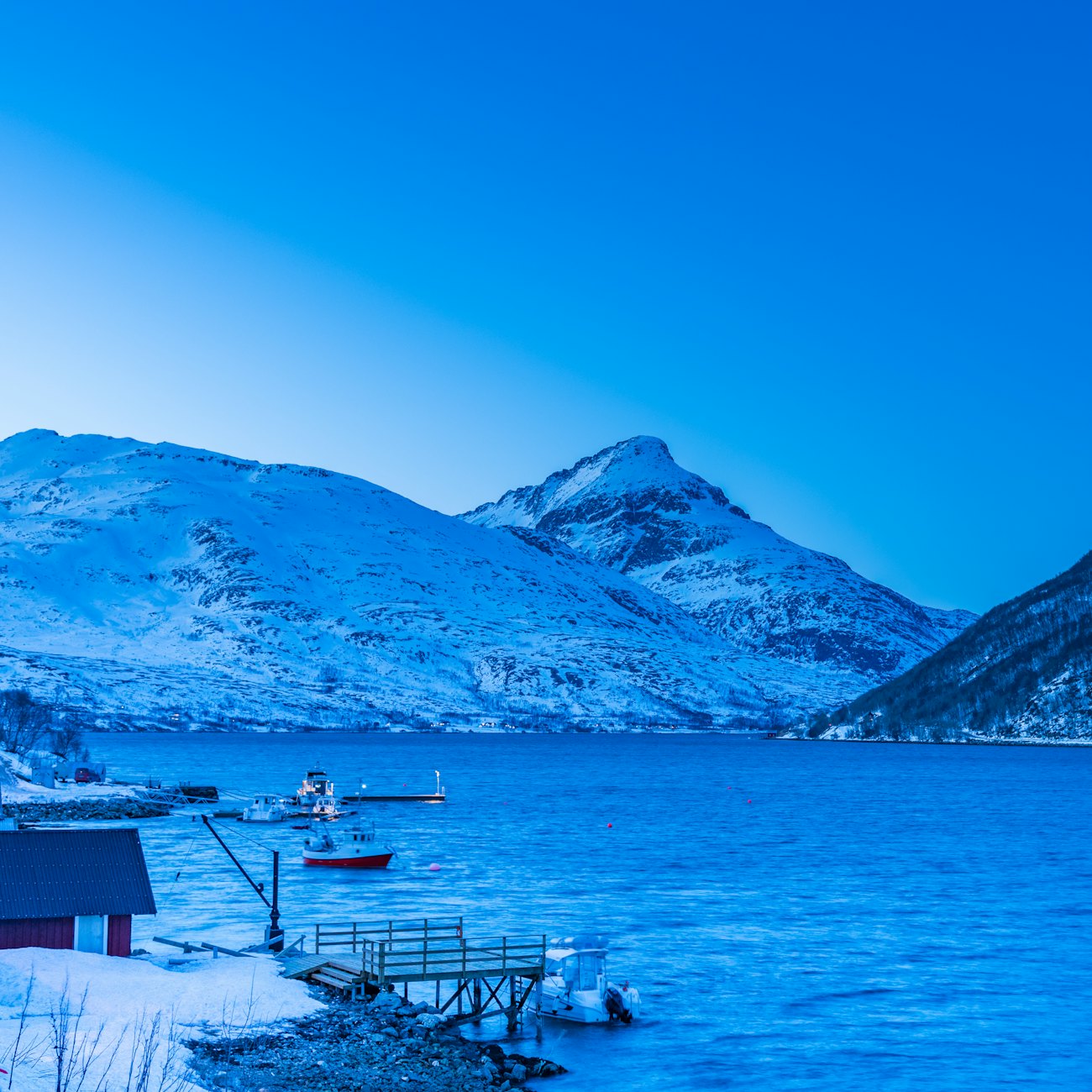 Snow-covered mountains and small fishing boats on a deep blue fjord