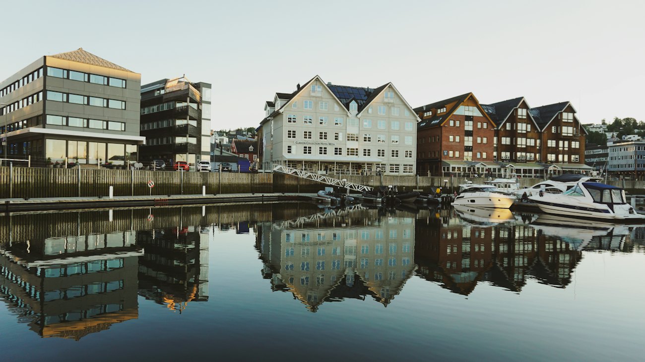 Wooden harbour-front buildings and moored boats reflected in calm water in Tromsø