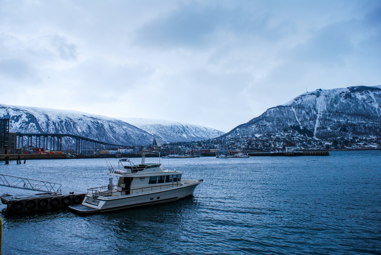 A boat moored in Tromsø harbour with the bridge and snow-covered mountains behind