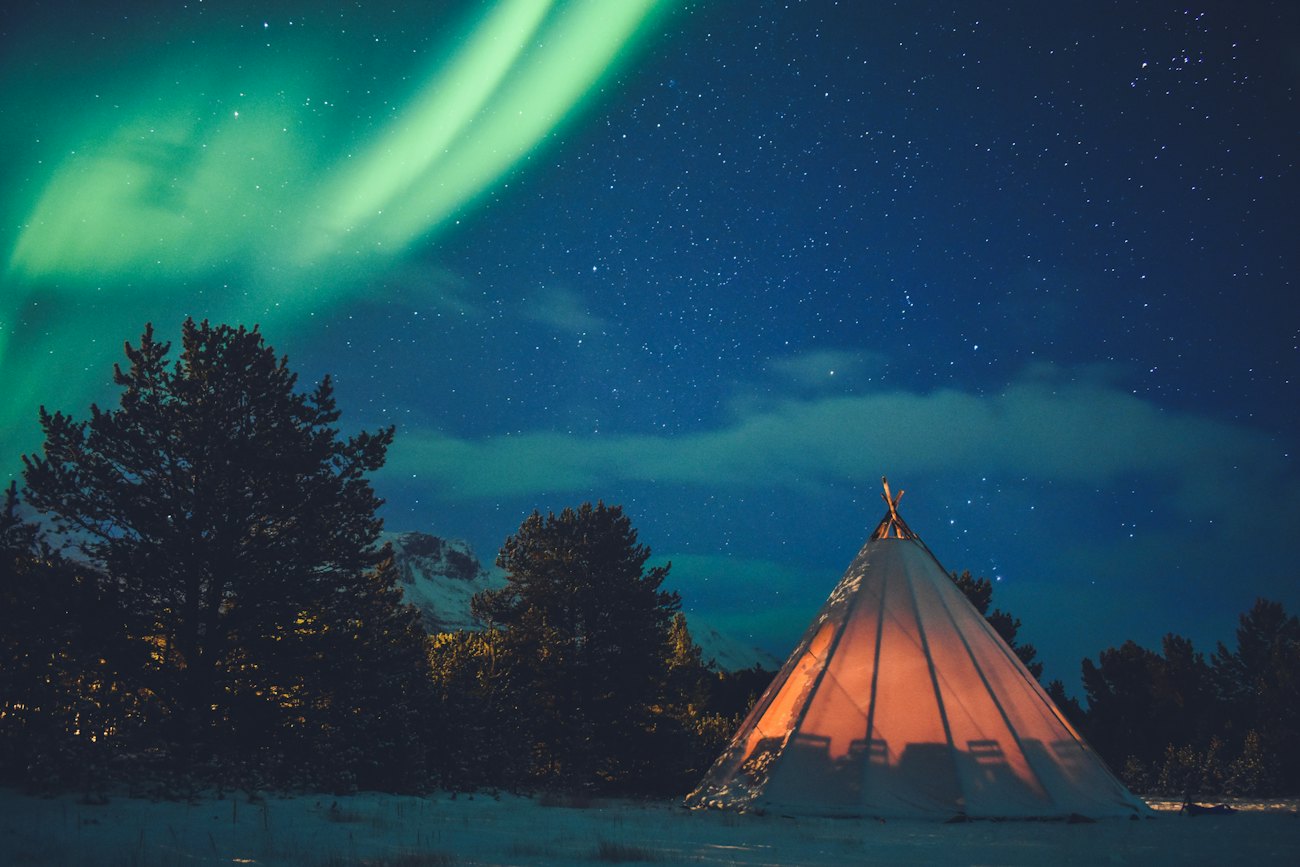 A glowing lavvu tent under green northern lights