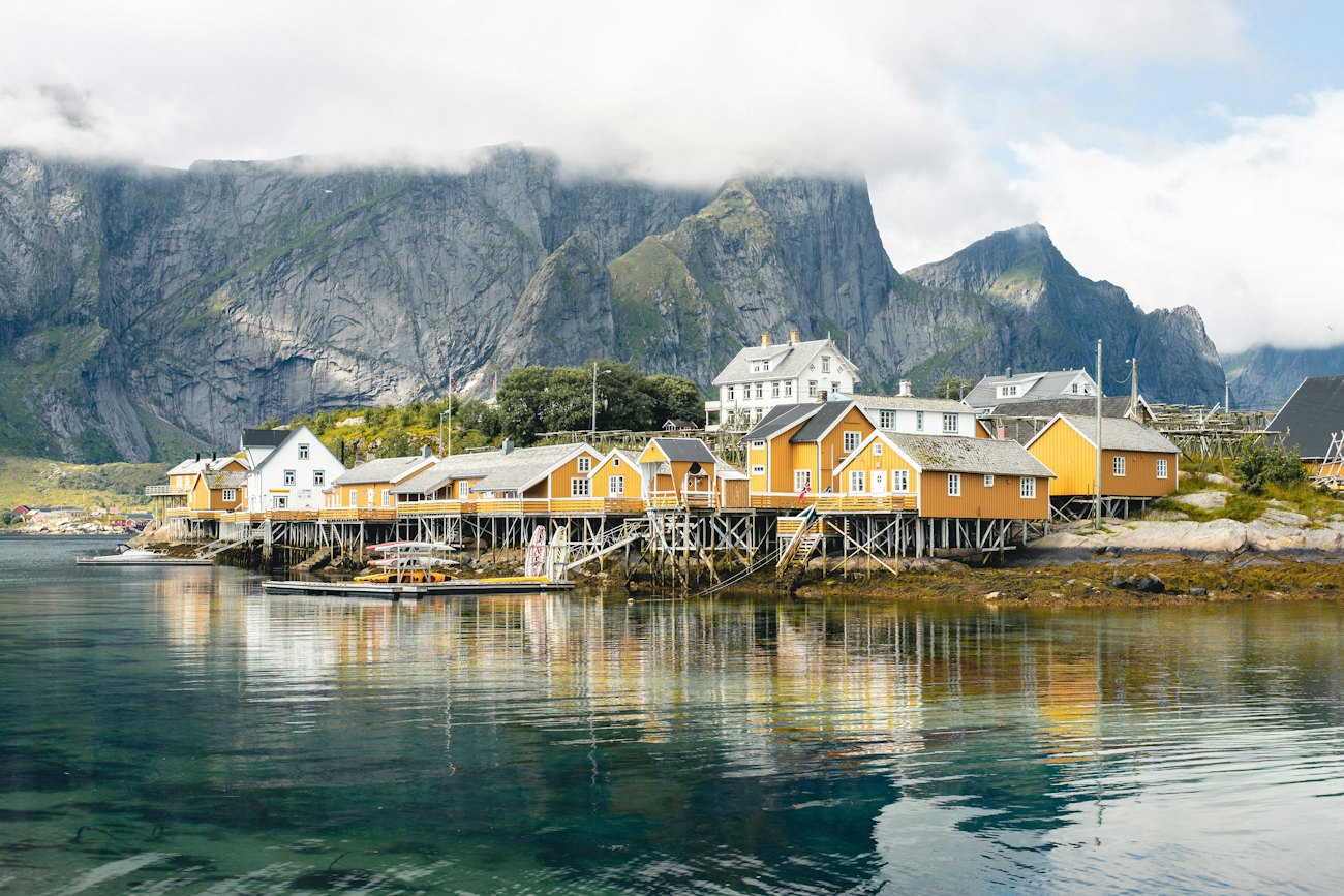 Yellow rorbu cabins on stilts reflected in calm green water at Sakrisøy