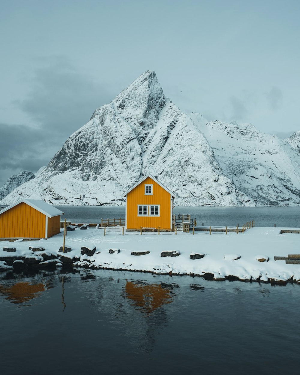 Yellow wooden cabins in the snow beneath a steep white mountain at Sakrisøy in Lofoten
