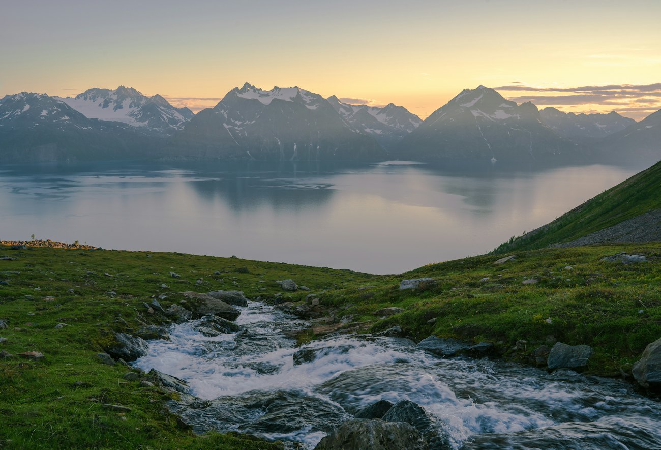 A mountain stream running down green slopes to the fjord with the Lyngen Alps behind