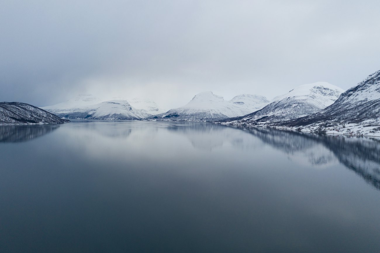 Snow-dusted mountains mirrored in a still, misty fjord