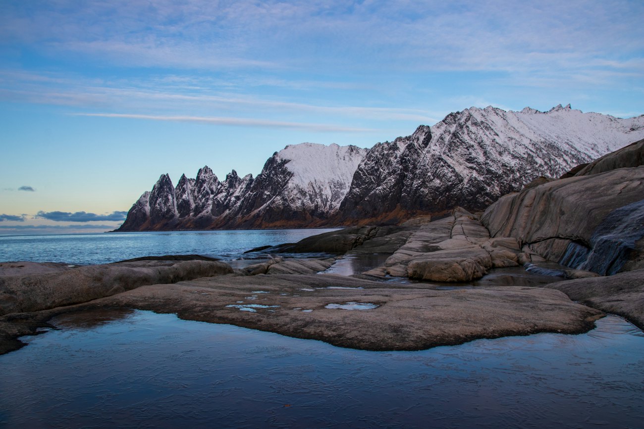 The jagged snow-covered Okshornan peaks seen across the water from the rocks at Tungeneset on Senja