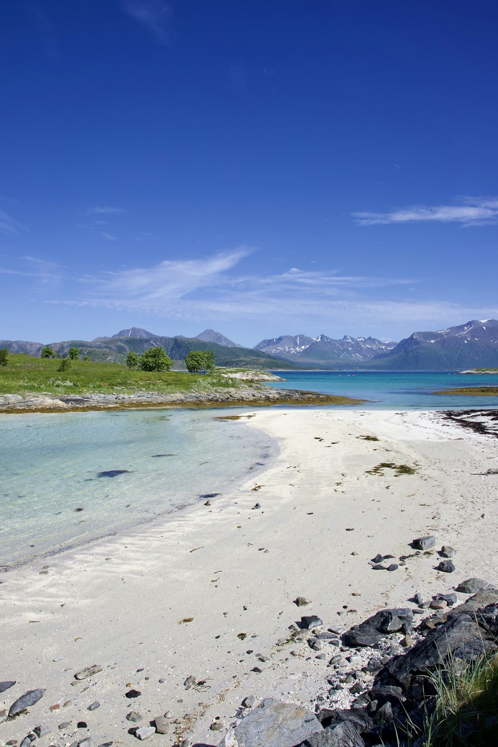 White sand beach and clear shallow water with mountains beyond