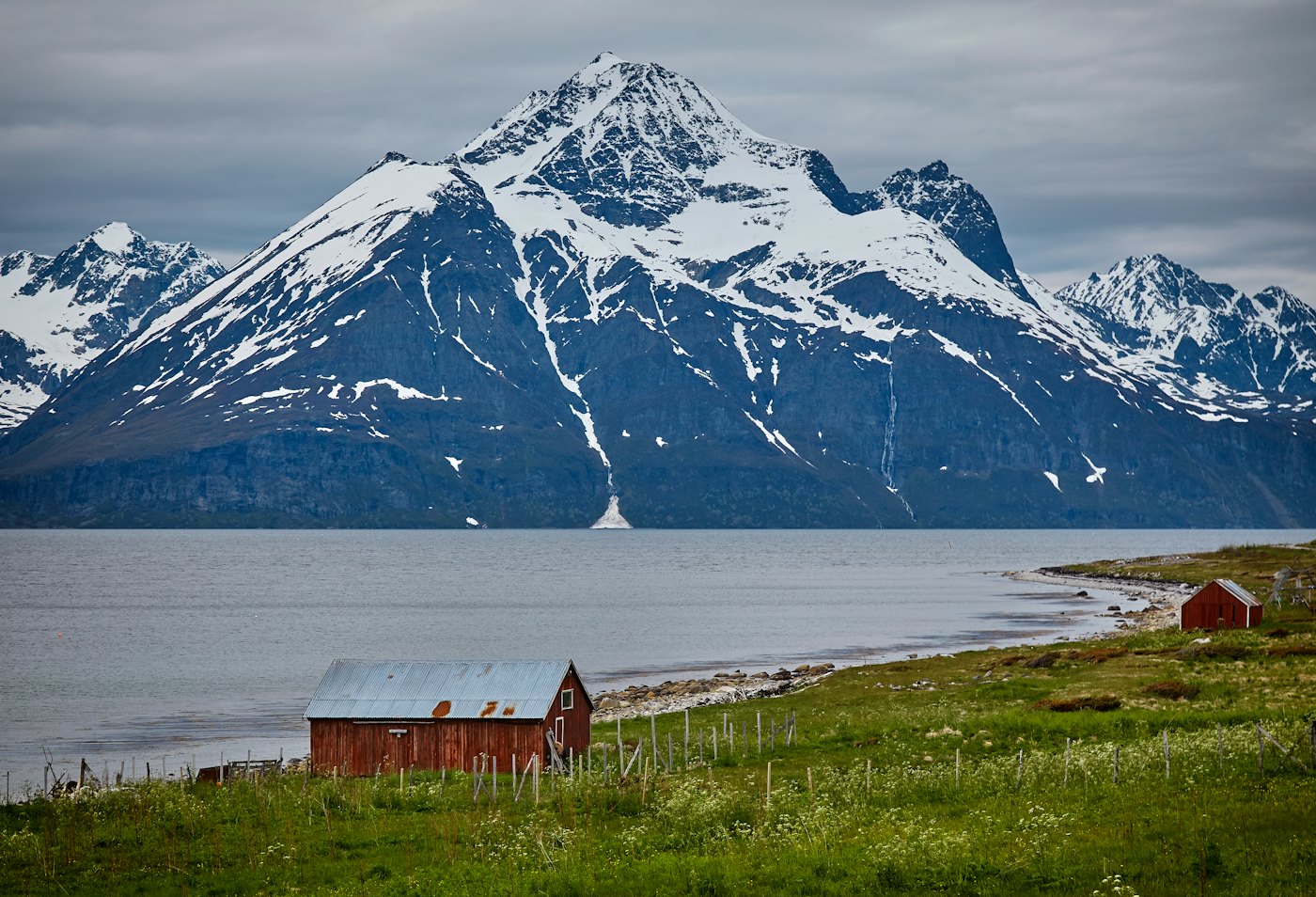 Snow-covered Lyngen Alps rising above a fjord with red barns on the shore